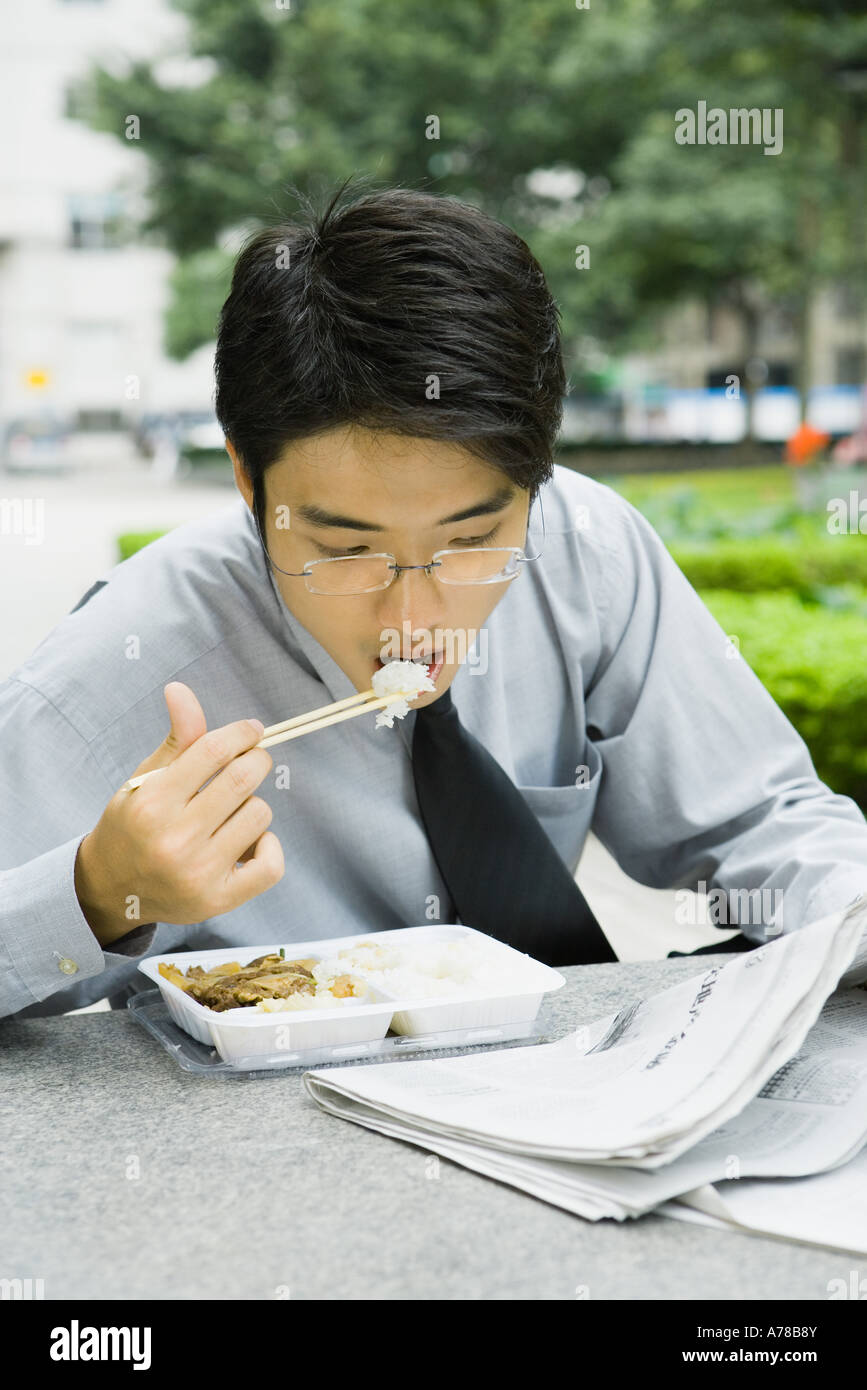Businessman eating lunch with chopsticks and reading newspaper Stock