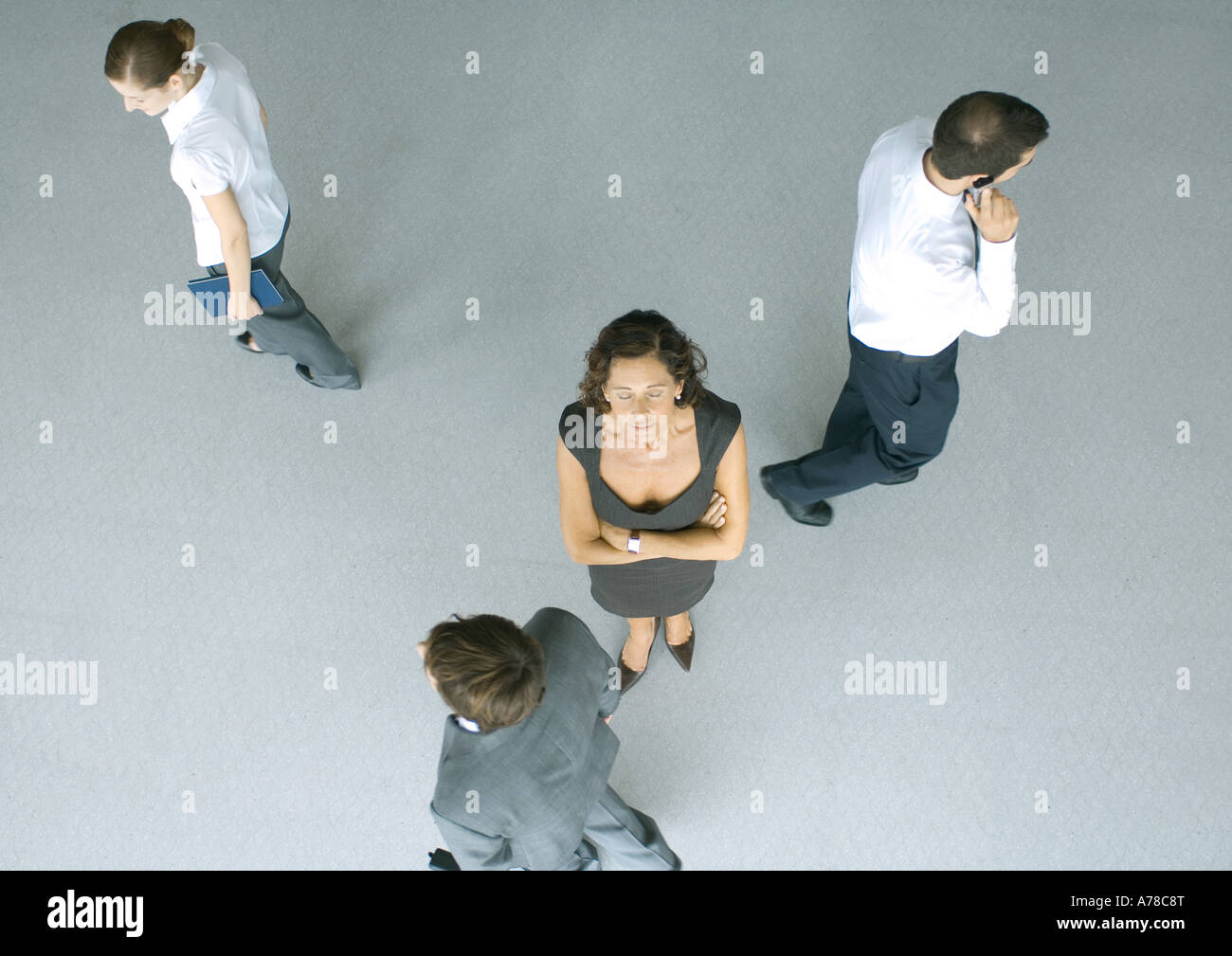 Mature businesswoman standing with arms folded and eyes closed, colleagues passing by, high angle view Stock Photo