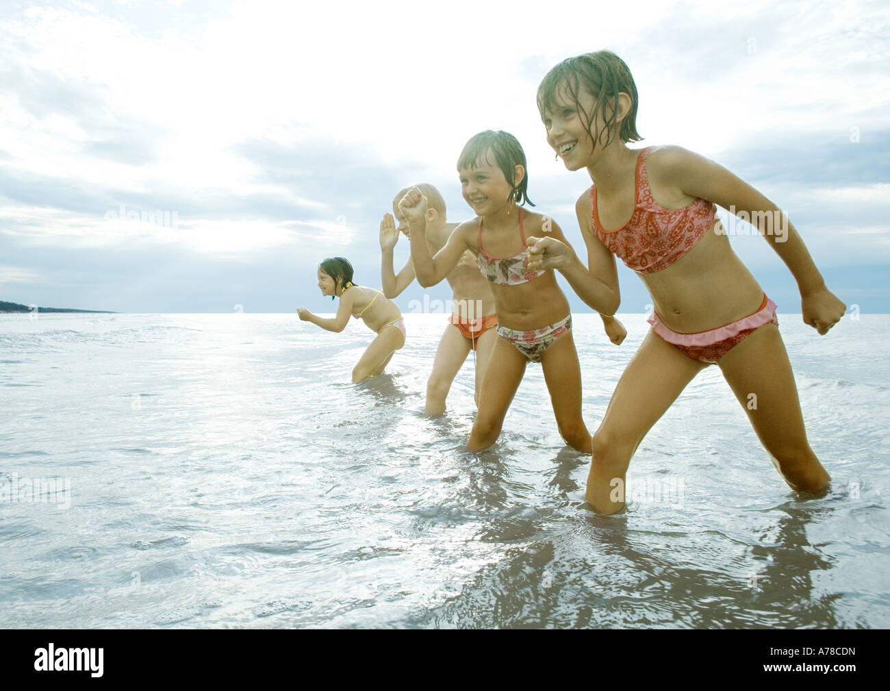 Four girls standing in shallow water, posed to race Stock Photo