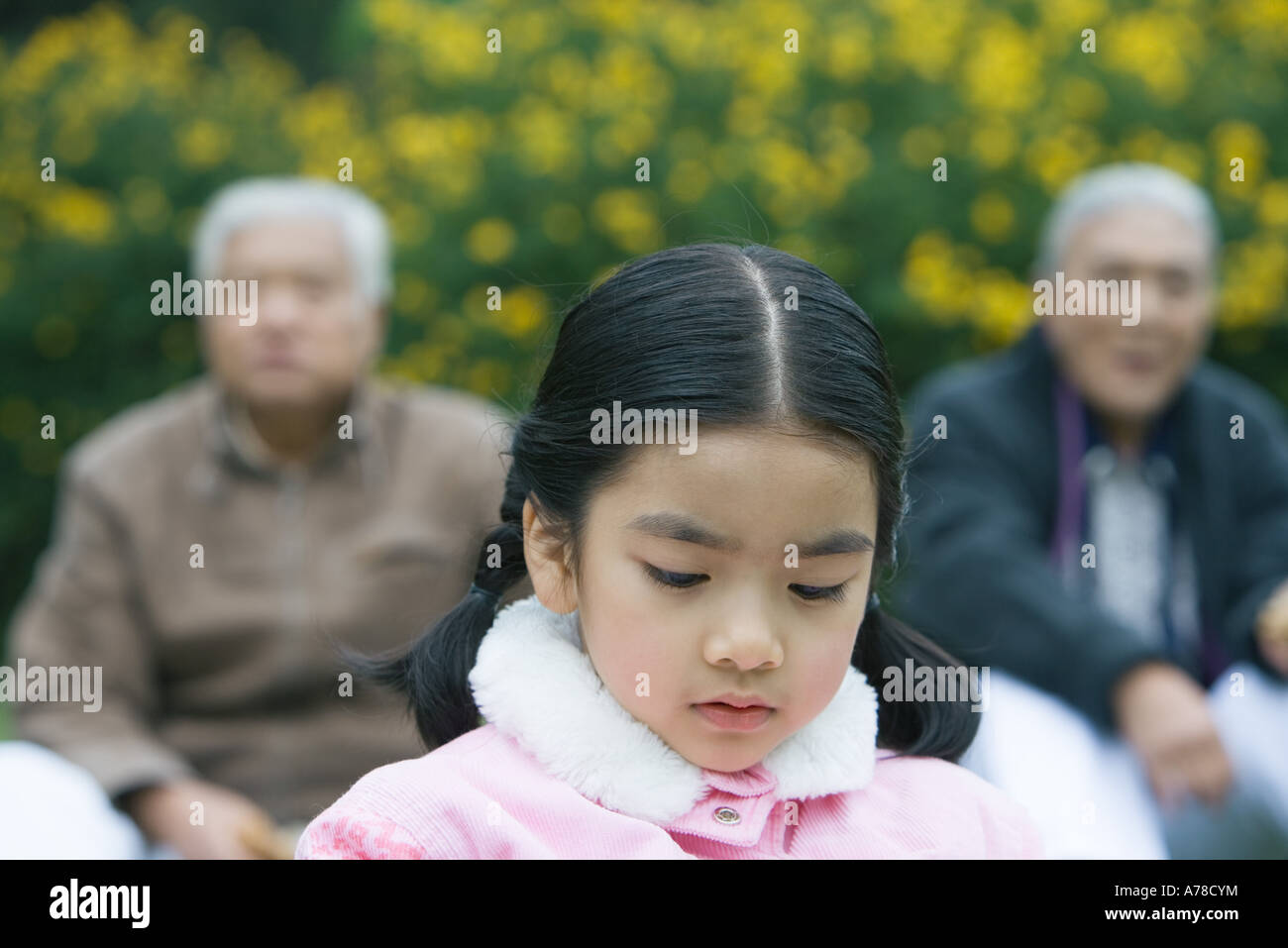 Girl looking down, grandparents in blurred background Stock Photo
