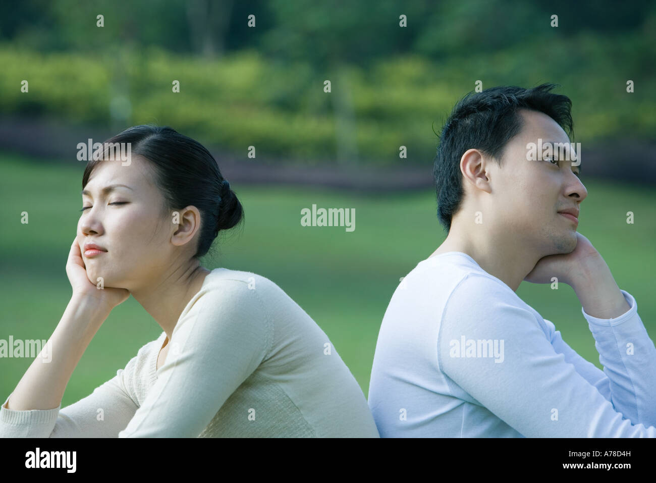 Couple sitting back to back, resting heads in hands Stock Photo