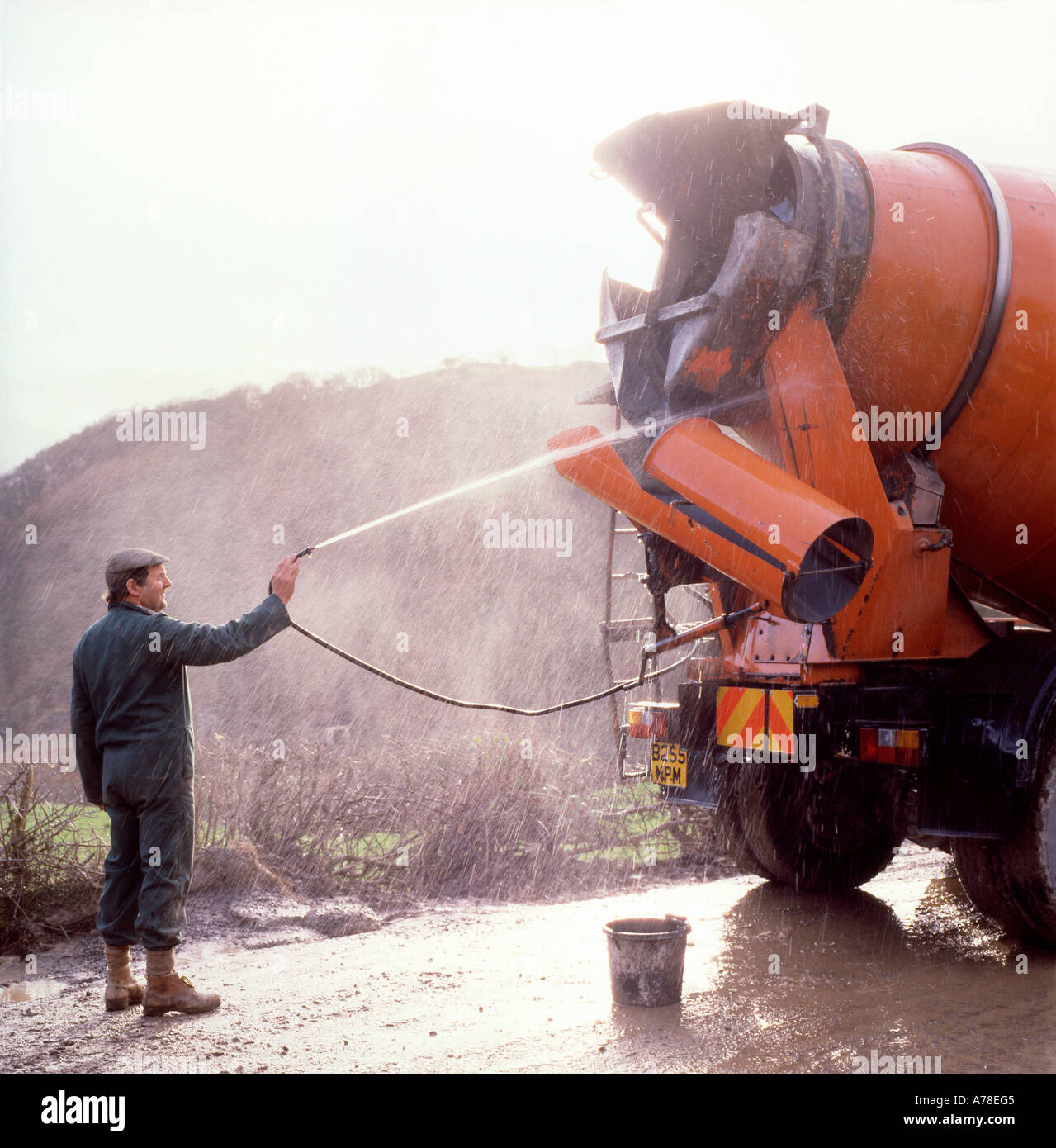 A man construction worker cleaning a cement mixer wash washing lorry