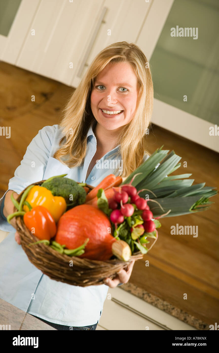 smiling woman in kitchen holding basket with organic vegetables fruit ...