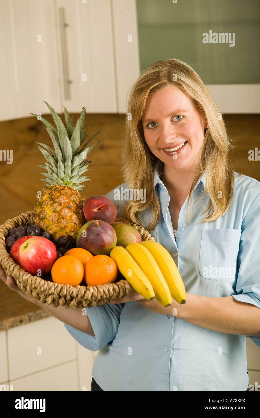 smiling woman in kitchen holding basket with organic vegetables fruit ...