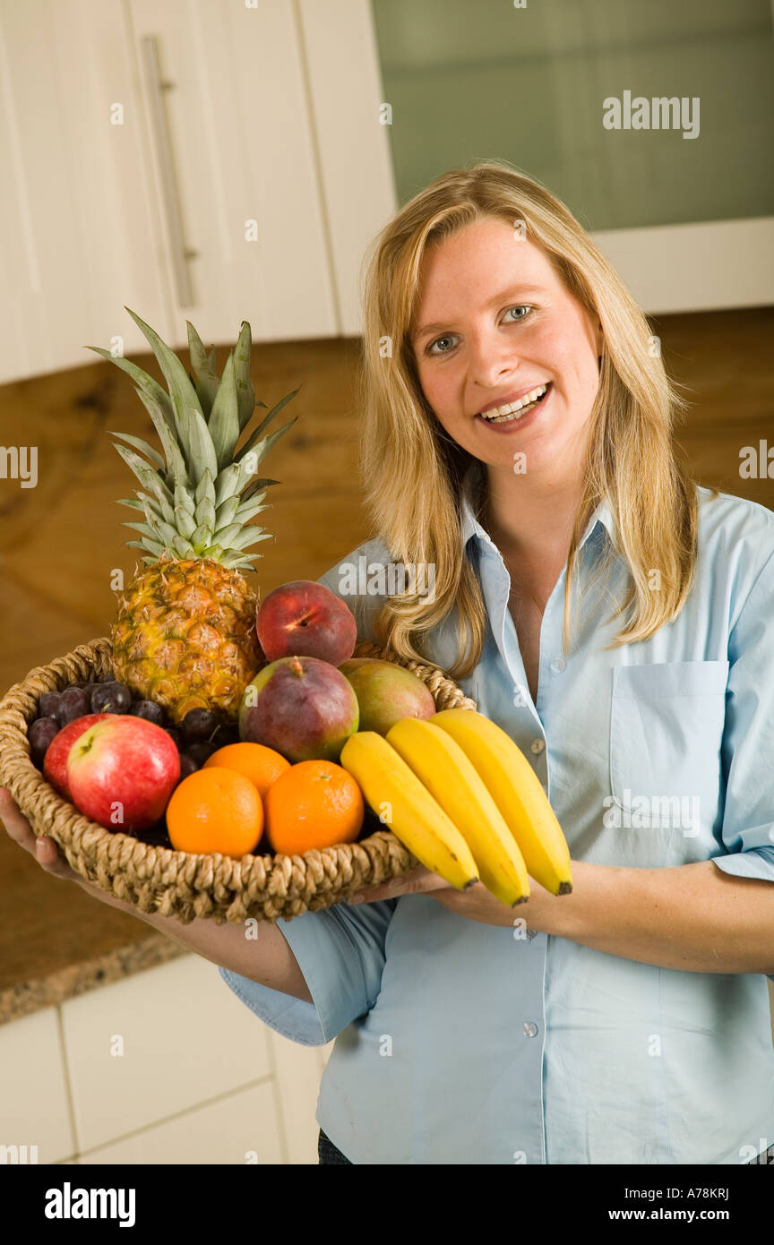 smiling woman in kitchen holding basket with organic vegetables fruit ...