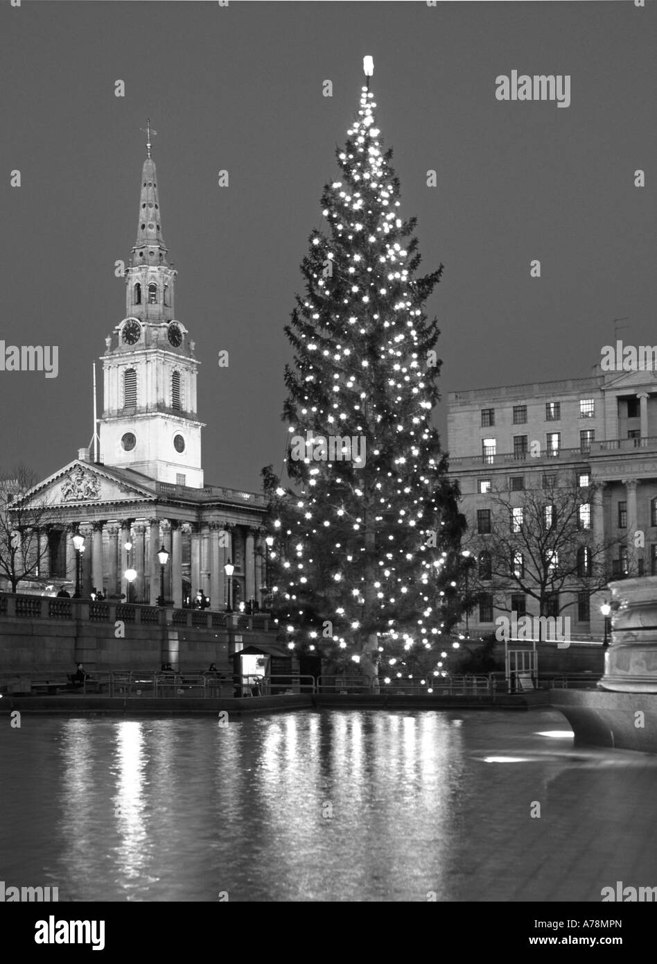 Reflections in water feature Trafalgar Square London England UK & Christmas tree lights with floodlights on St Martin in the Fields church & spire Stock Photo