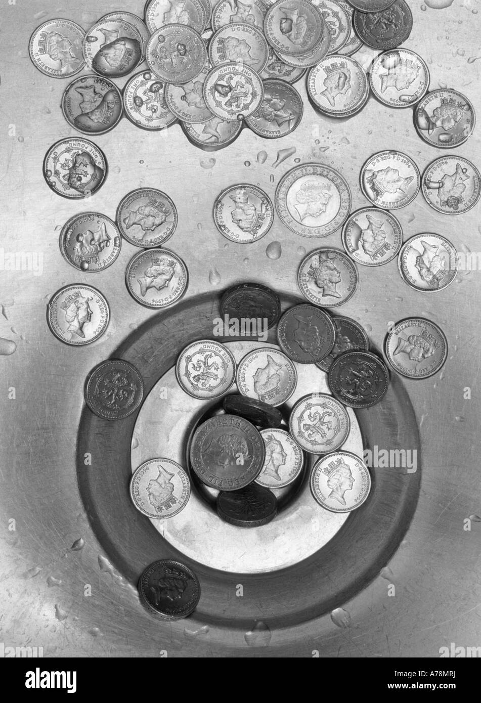 Money down the drain concept image with pound sterling coins around stainless steel sink bowl waste outlet Stock Photo