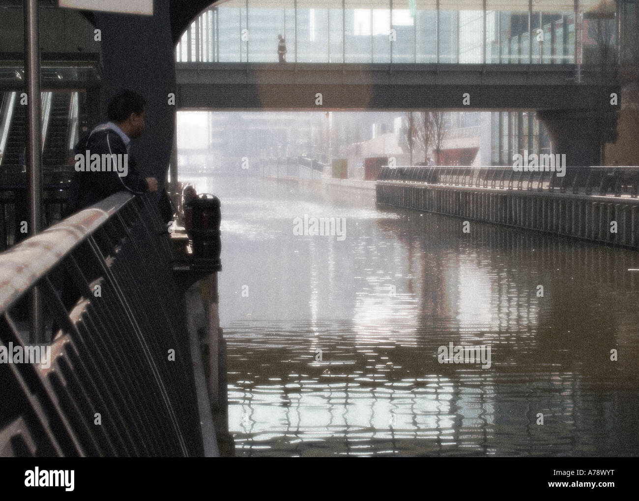 CHURCHILL PLACE.  Man in foreground, looking at water, whilst man crosses  it in background. Diffuse glow filter used on image. Stock Photo