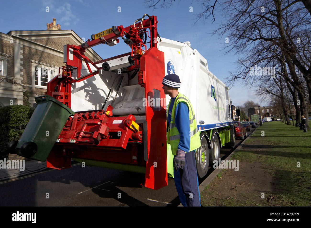 Waste rubbish or trash lorry or truck lifting green bin with man in