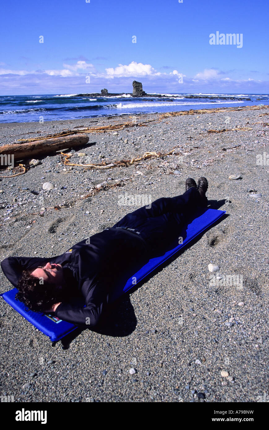 A man 20 25 takes a break from hiking at Bonilla Point on the West Coast Trail near Carmanah Creek in Pacific Rim National Park Stock Photo