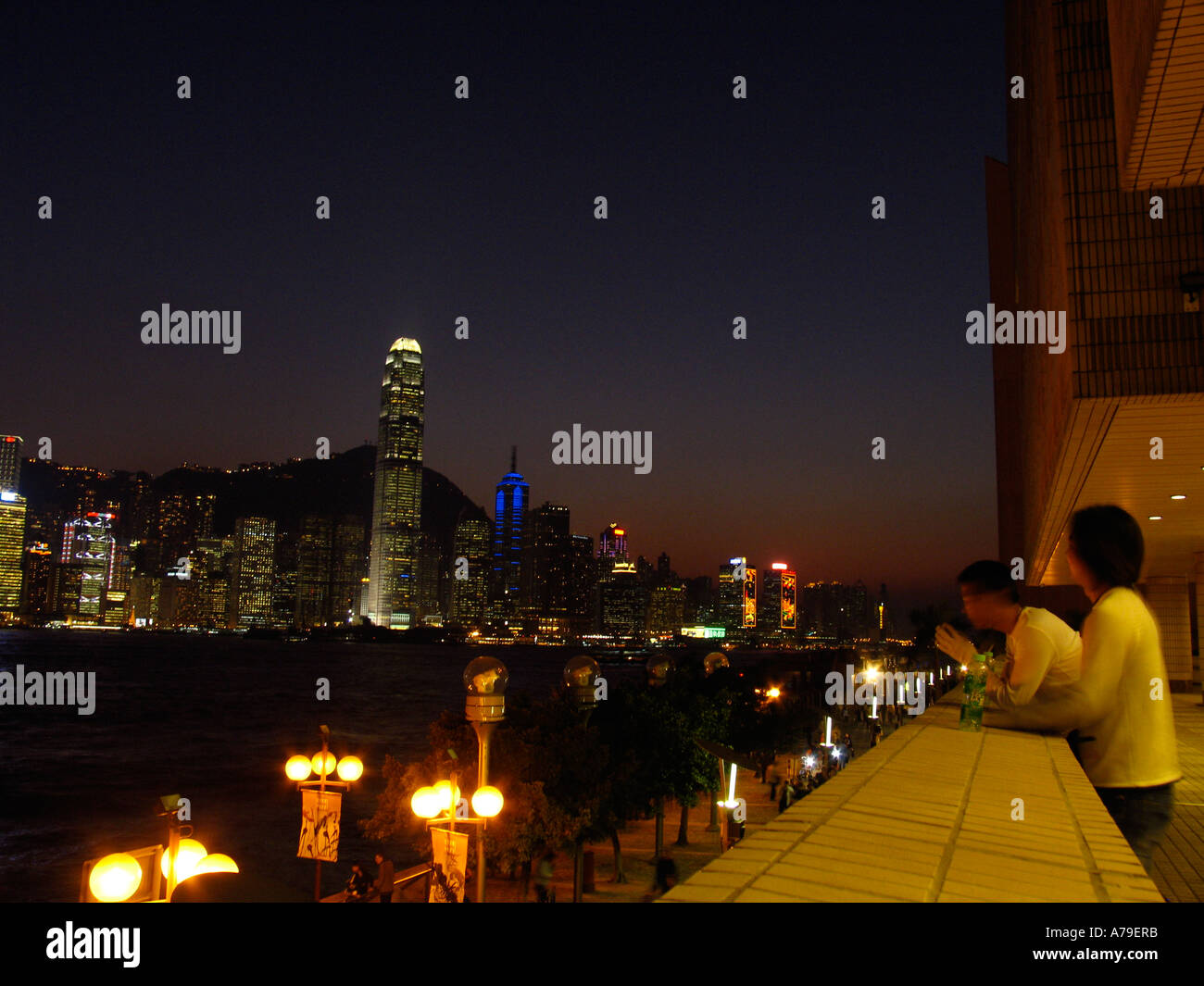 Men looking in the evening from Kowloon at Victoria Harbour and the skyline of Hongkongs Central District Stock Photo
