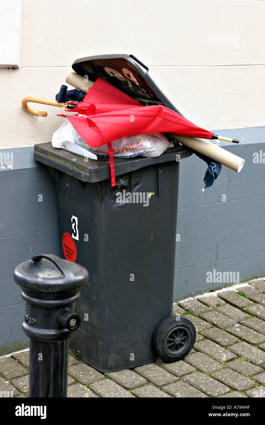 A bright red but broken umbrella lies at the top of a rubbish trash bin