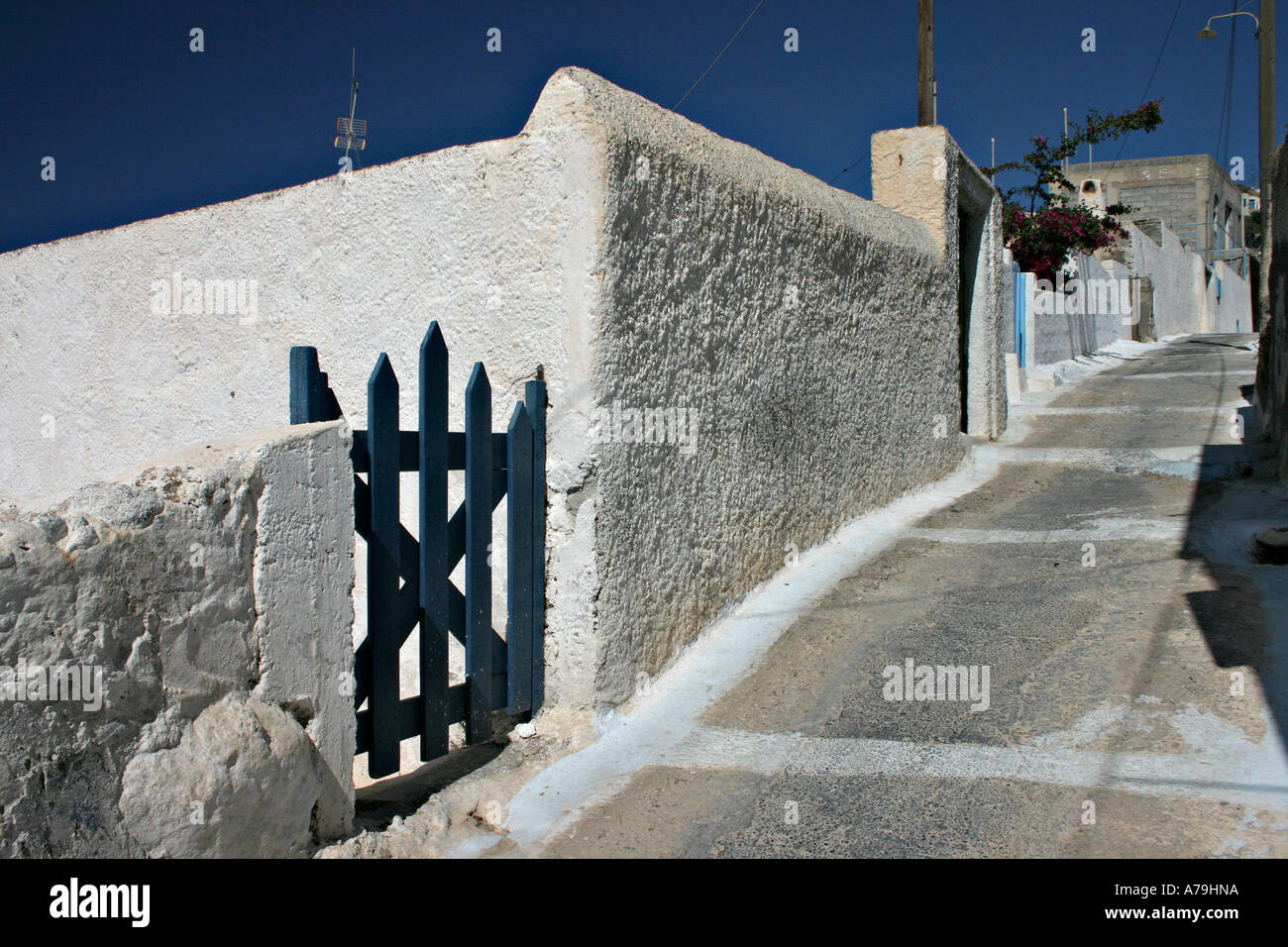 A dark blue gate along an siesta emptied and sloping street of a typical cyclades village Acrotiri Santorini Greece Stock Photo