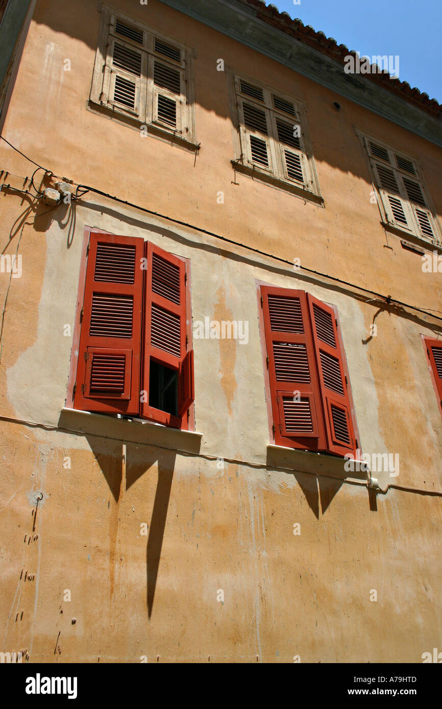 Shuttered against the Sun: The wall of an old building in Nafplio Red shutters shade the windows from the bright morning sun Stock Photo
