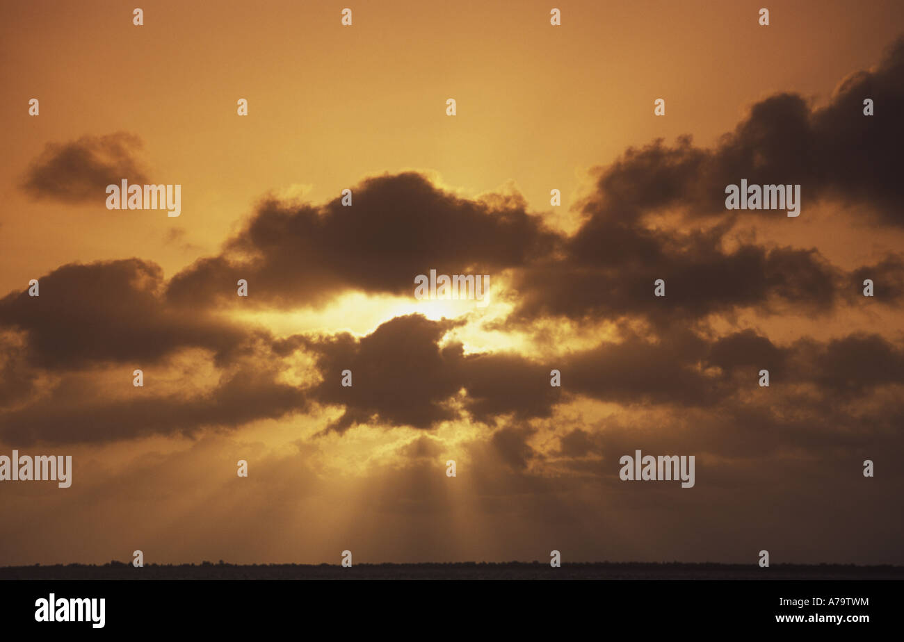 An orange sunset fills the sky and creates sunbeams through  clouds. Stock Photo