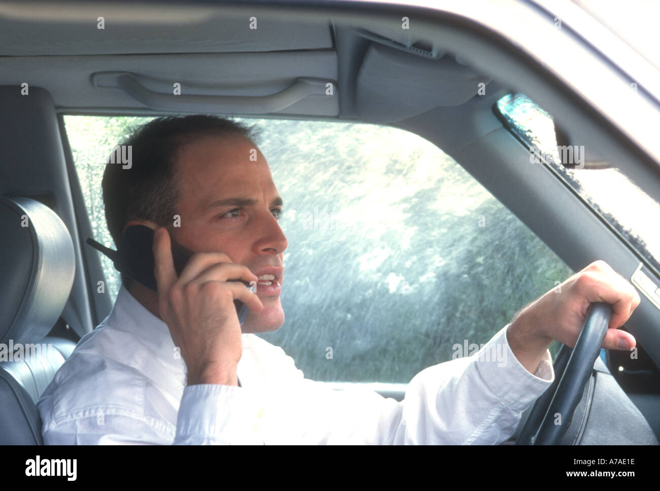 businessman talking on cell phone while driving car in rain Stock Photo
