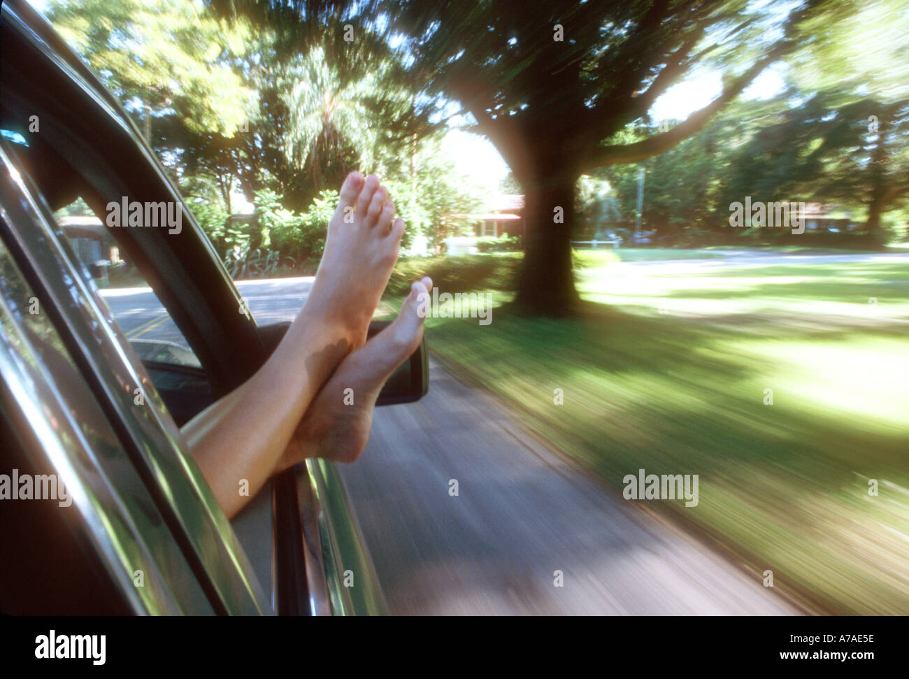 teenage girl sticking her bare feet out the window of a moving car