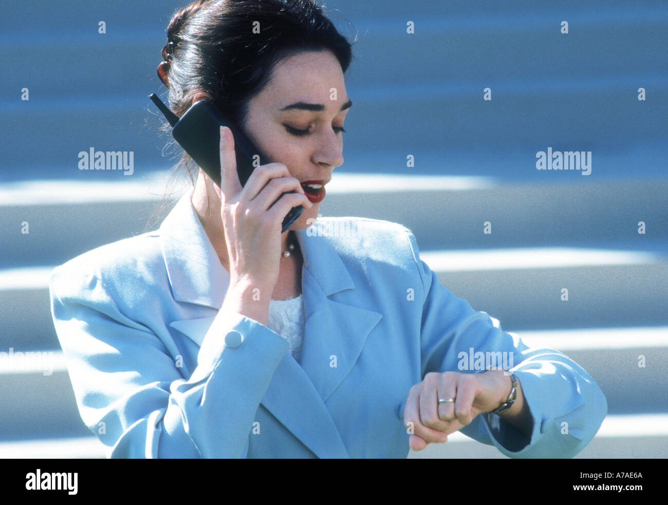 woman executive checking watch while talking on a cell phone on steps of an office building Stock Photo