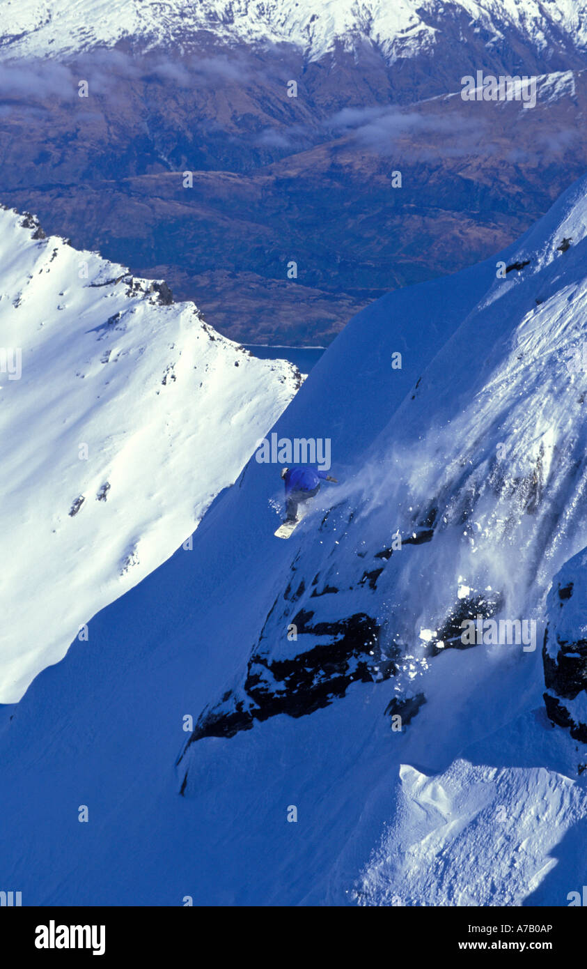 Dramatic image of a snowboarder off piste coming off a near vertical rock outcrop back country New Zealand Stock Photo
