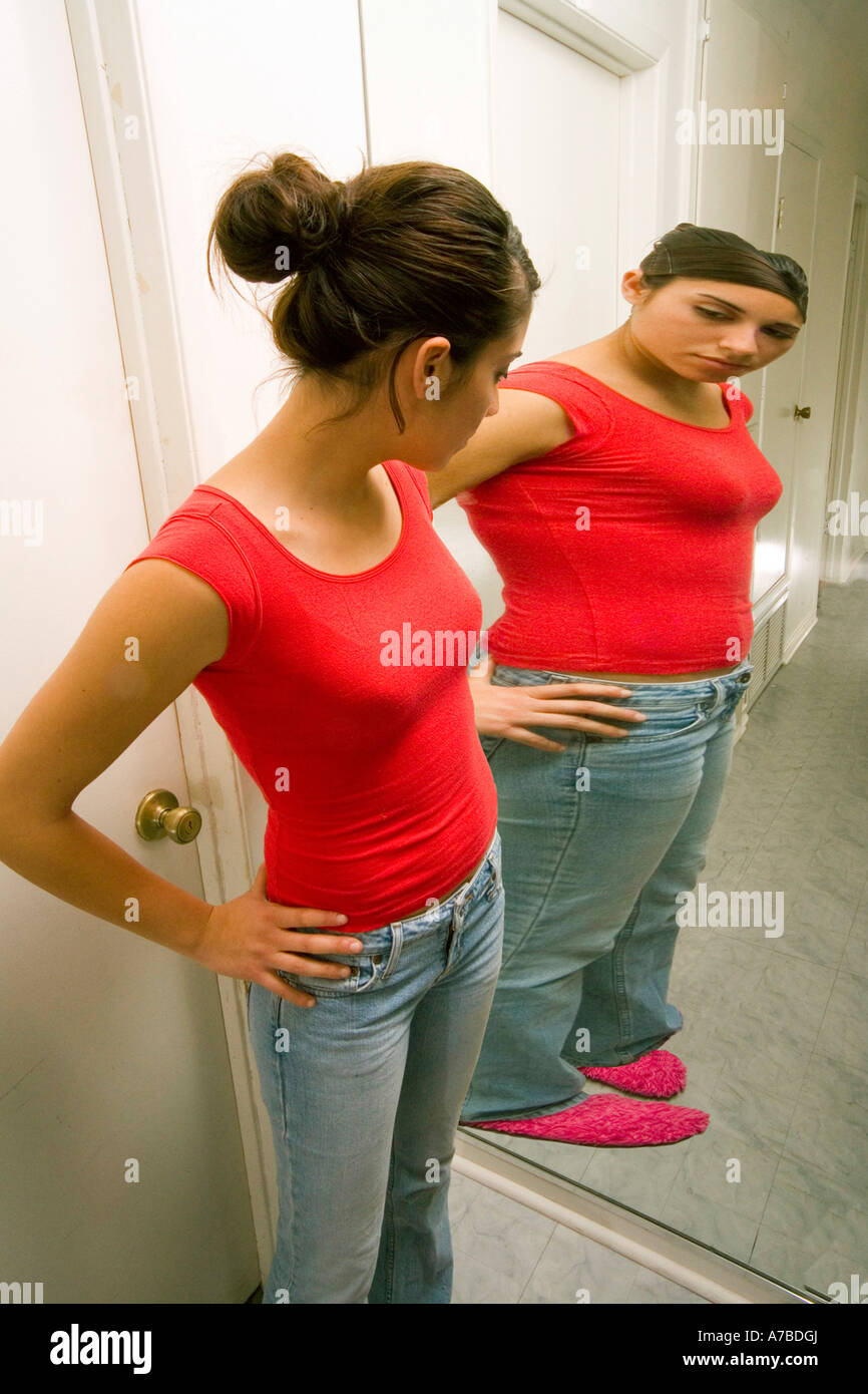 Hispanic teen girl sees herself as overweight in reflection in mirror Model released Stock Photo