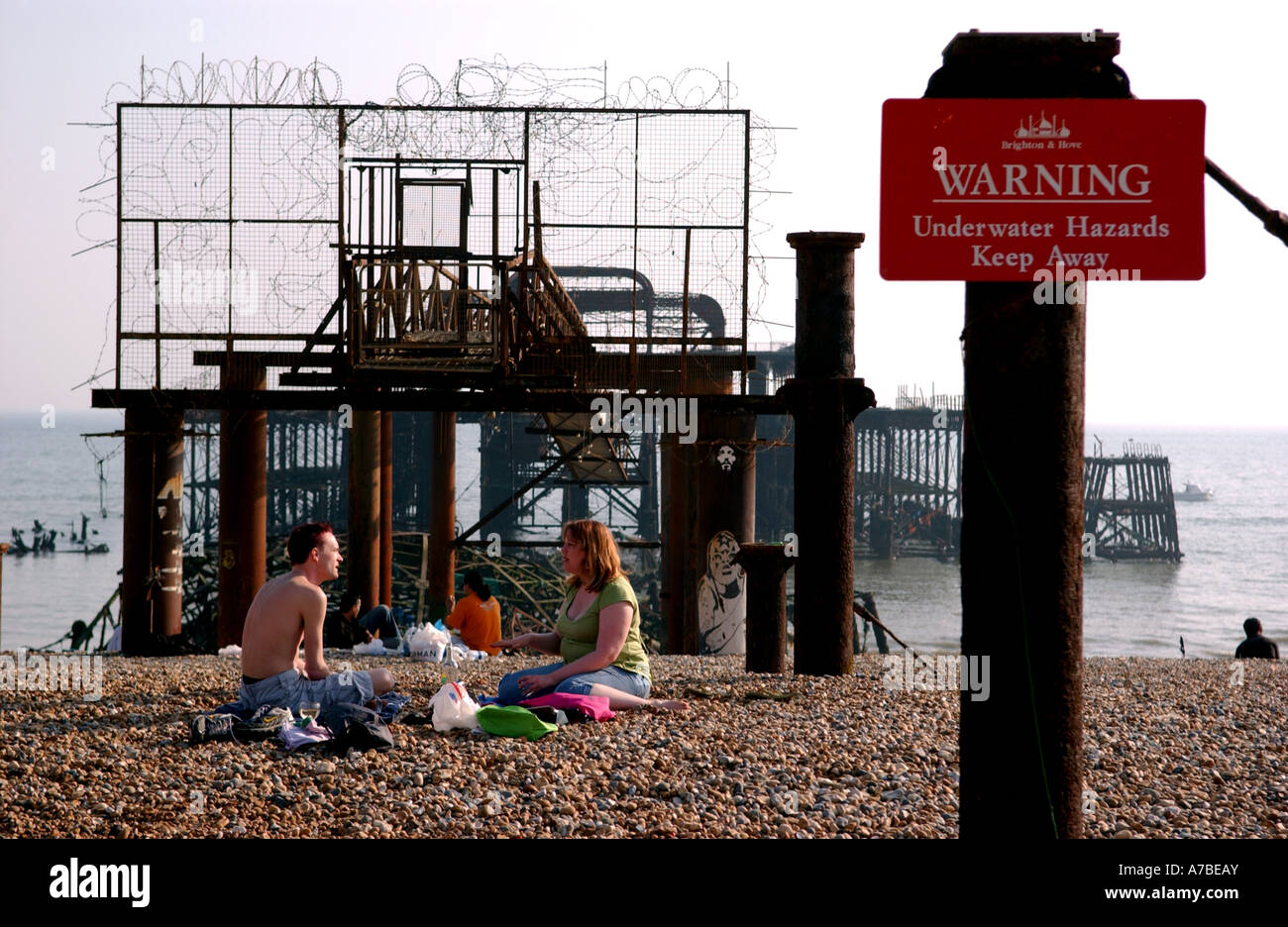 A couple enjoy the hot weather against the unusual backdrop of the derelict West Pier in Brighton UK Stock Photo