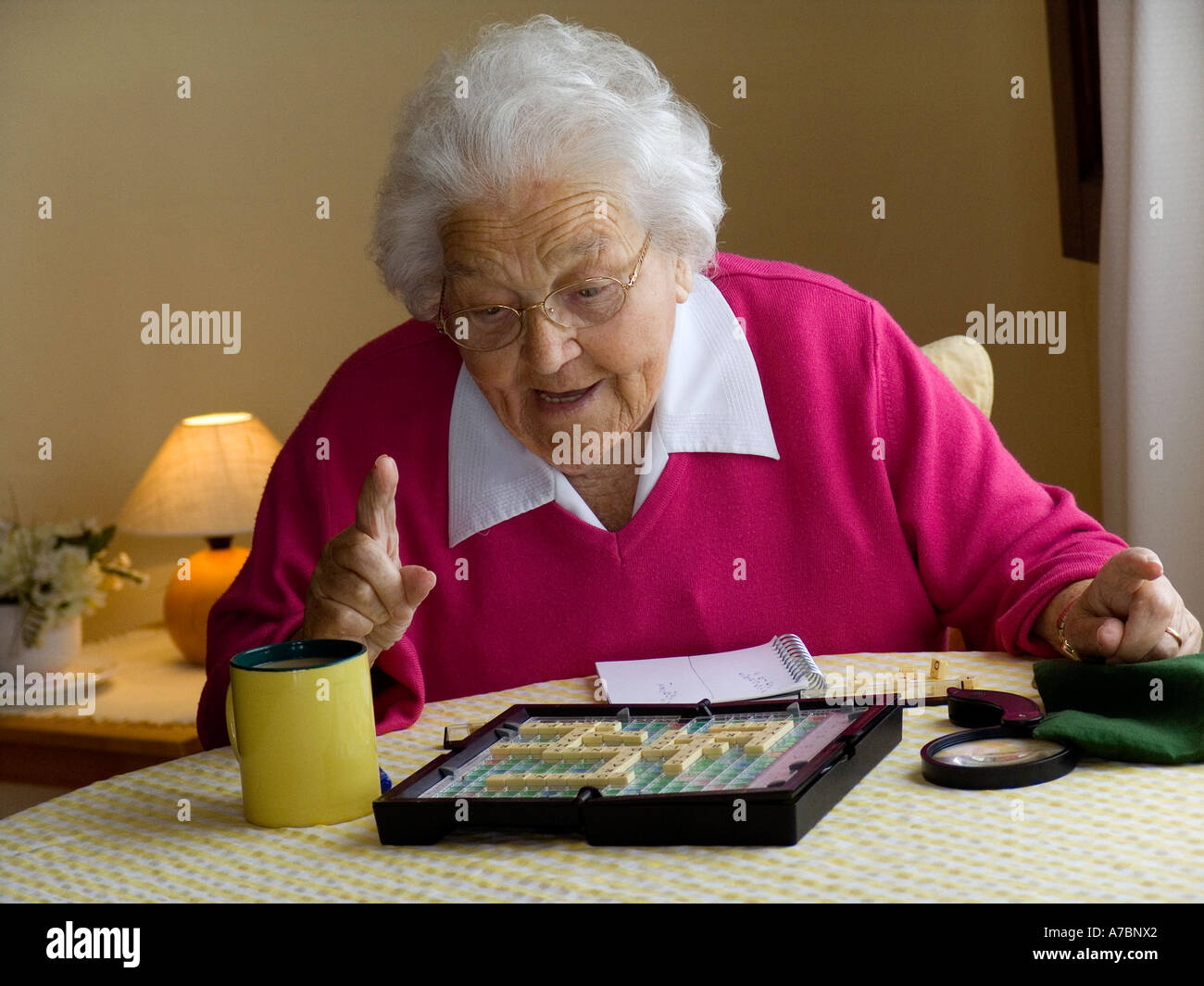 Elderly lady  keeping her mind alert by playing single scrabble word game at living room table in natural window light Stock Photo