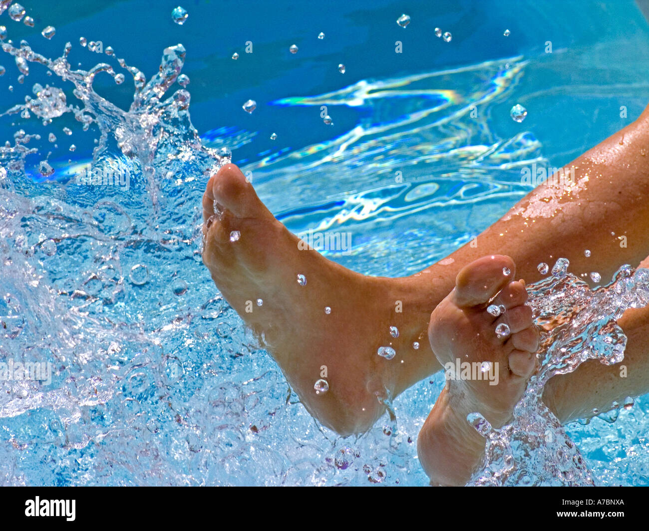 Woman's feet splashing the clear water in a sunny swimming pool Stock Photo