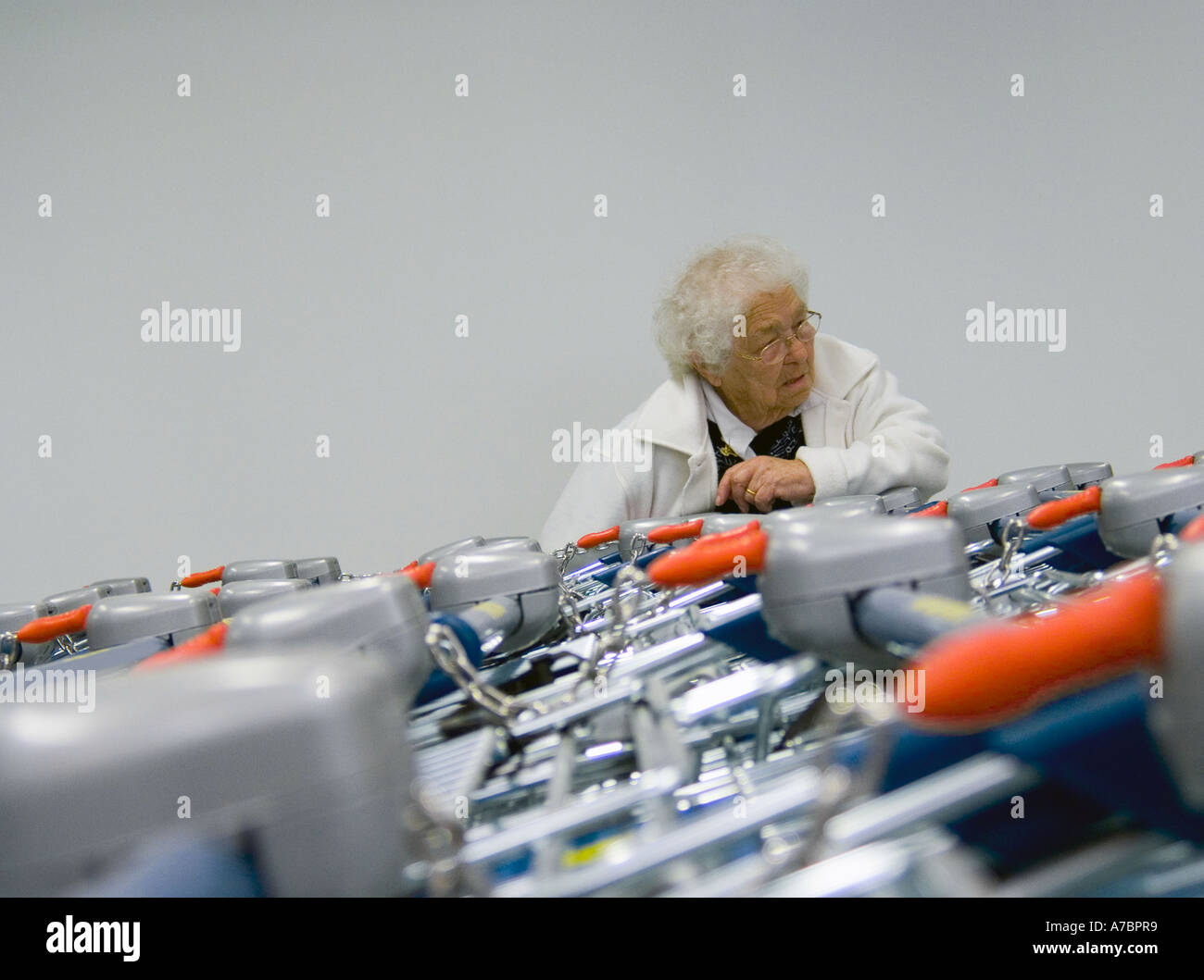Elderly woman gasping wheezing exhausted rests on row of supermarket shopping trolleys Stock Photo