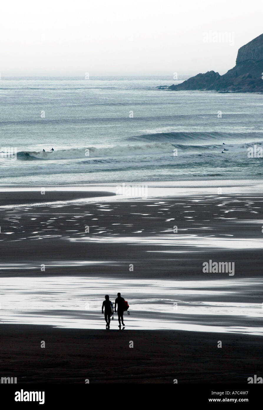 Two surfer silhouetted walking along beach Stock Photo