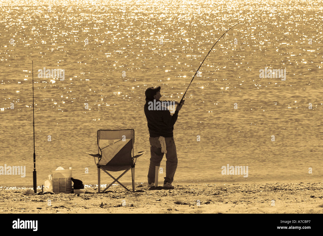 fisherman reeling in a fish from shore Stock Photo