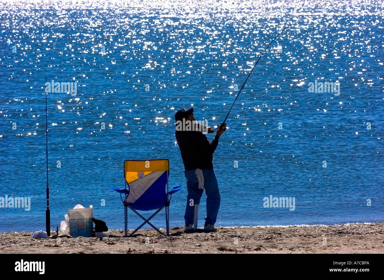 fisherman reeling in a fish from shore Stock Photo