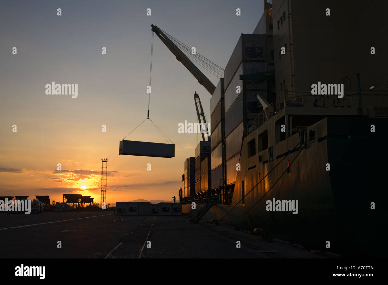 Unloading shipping containers at sunset from Cargo Ship silhouetted in