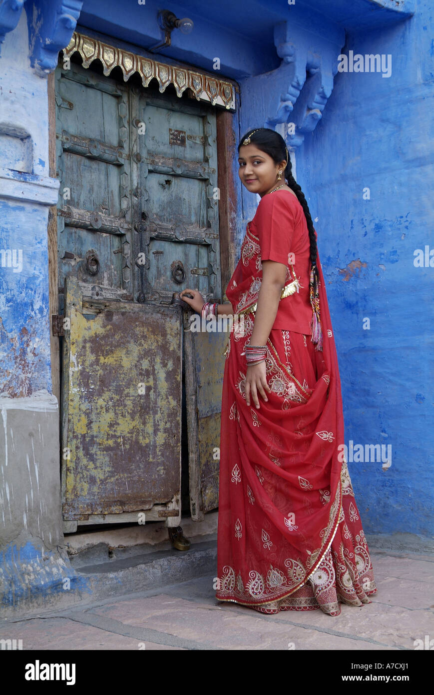 Woman wearing a red sari standing in front of an old door, in Jodhpur ...