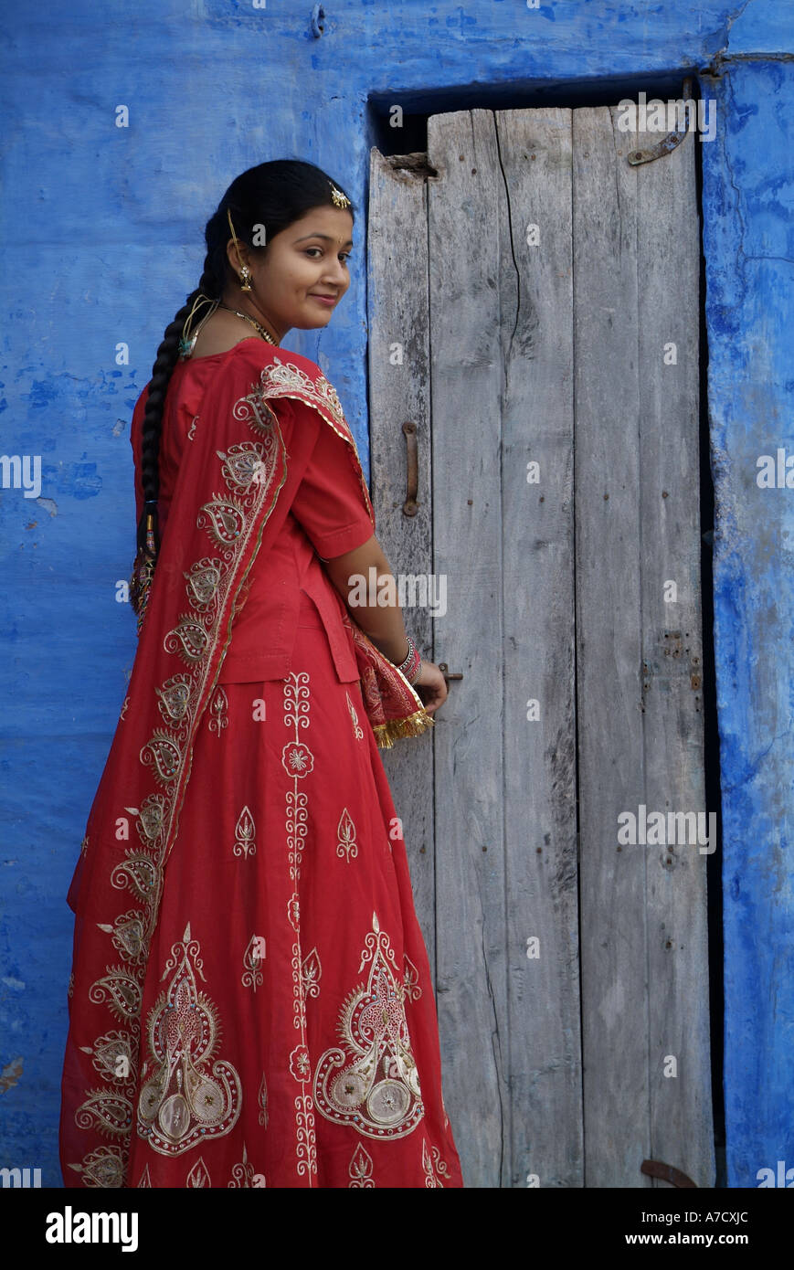 Woman wearing a red sari standing in front of an old door, in Jodhpur ...