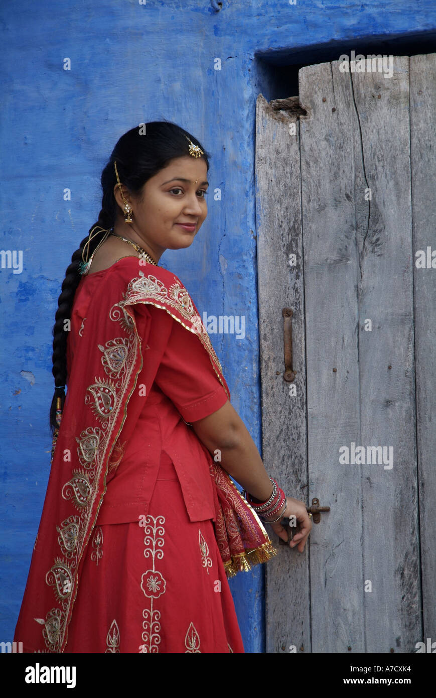 Woman wearing a red sari standing in front of an old door, in Jodhpur ...