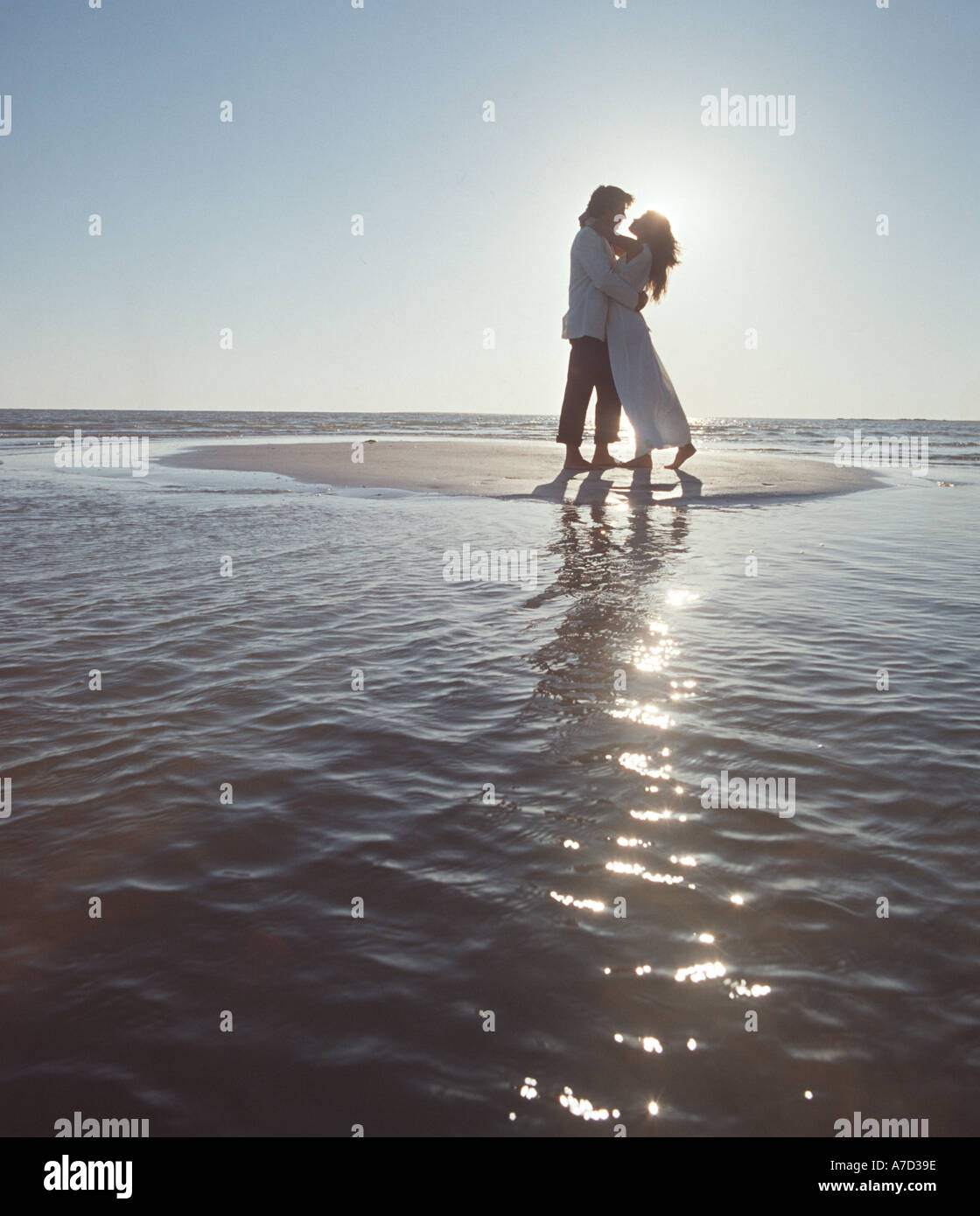 couple in formal clothing embracing on a tiny sandbar at the beach at sunset Stock Photo