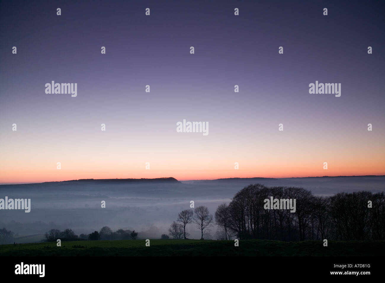 View of a rural landscape shrouded in fog at dusk with a corona of sunlight still visable in the sky, Dorset, UK Stock Photo