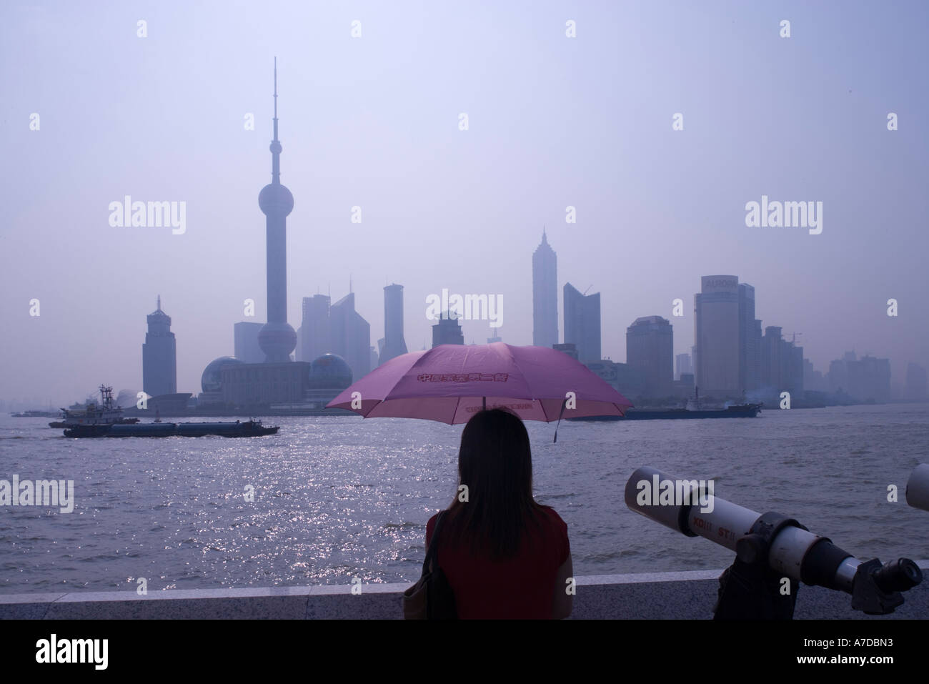 Asia China Shanghai Young woman looking across Huangpu River at Oriental TV Tower and and skyscrapers of Pudong skyline Stock Photo
