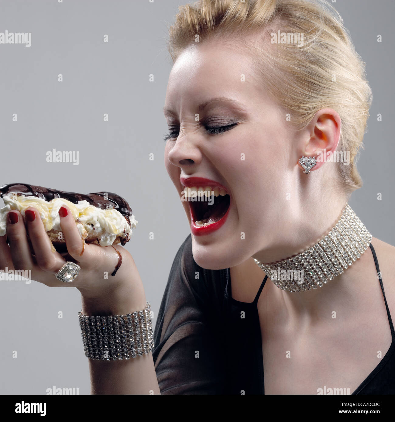 Glamourous greedy woman eating enormous eclair Stock Photo