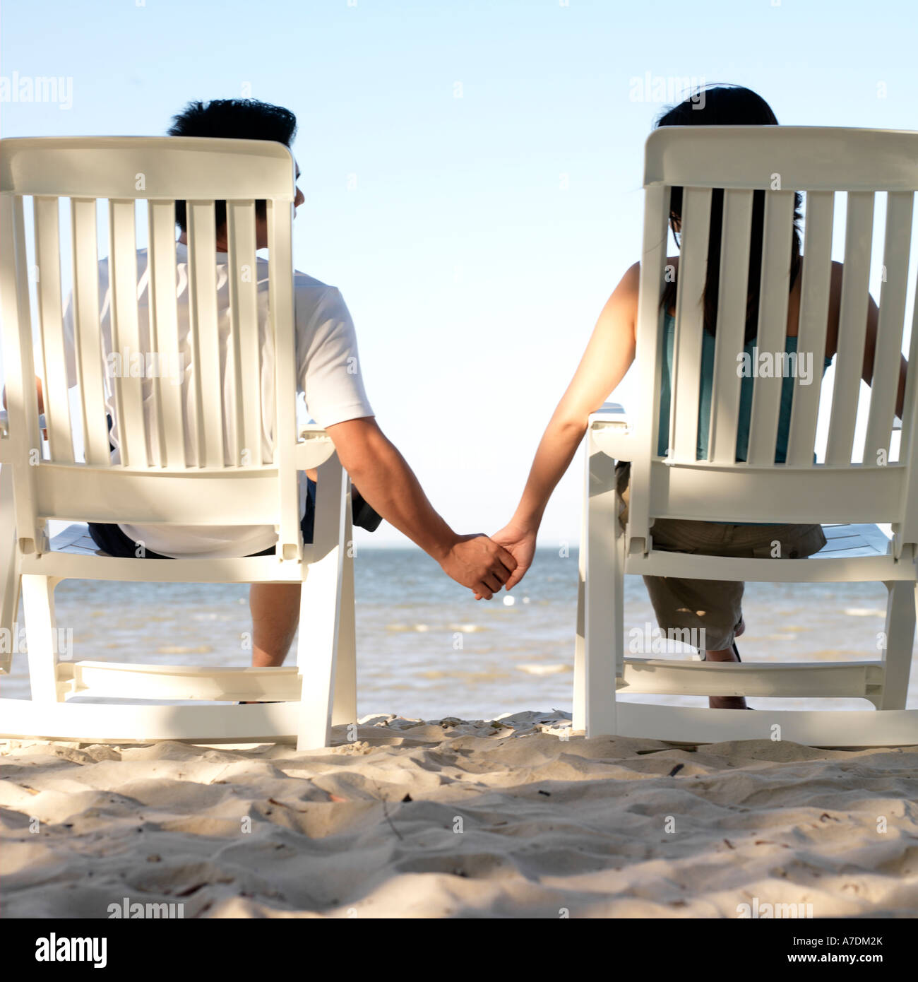 View of a couple holding hands in deck chairs on the beach Stock Photo