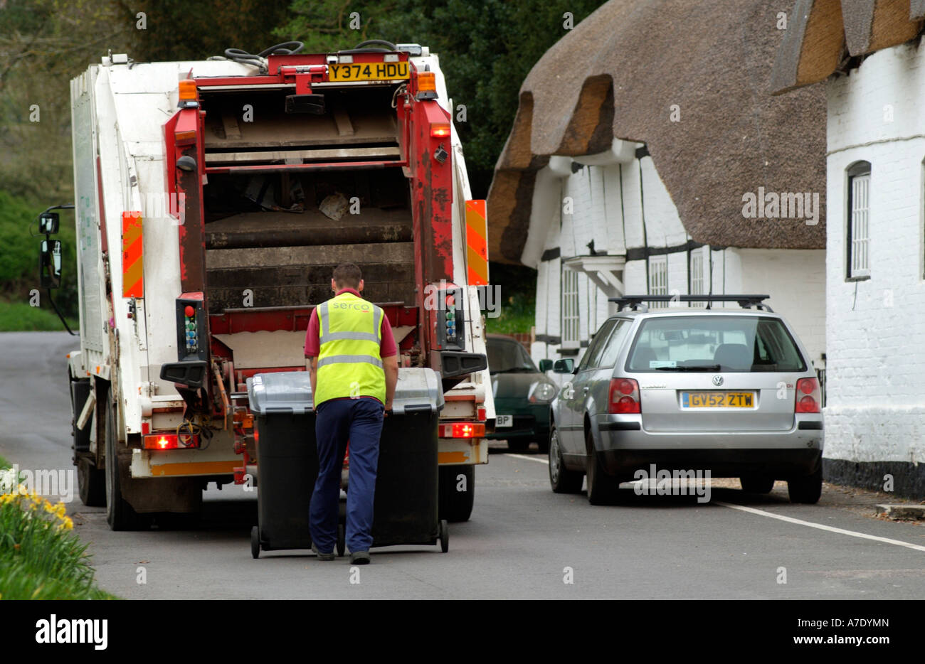 Refuse operative Dustman emptying wheelie bins onto a lorry in a rural location in Hampshire SERCO Stock Photo