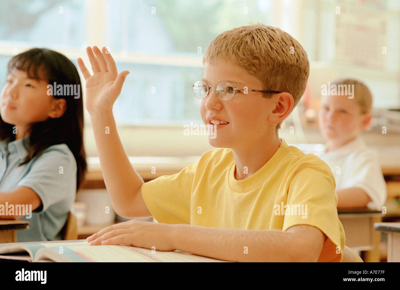 Eager boy raising hand in school classroom Stock Photo