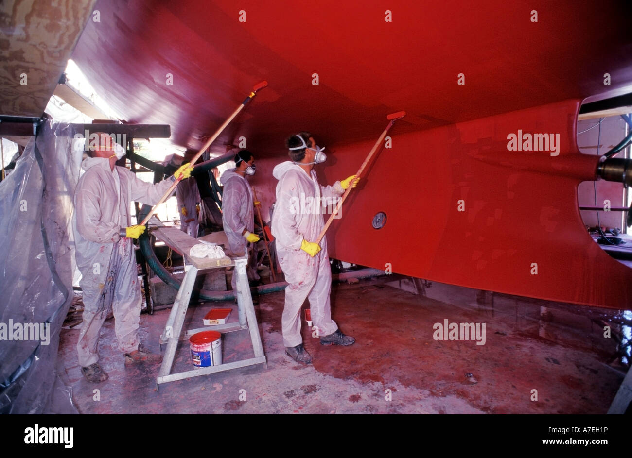 People wearing protective clothing painting the hull of a yacht with