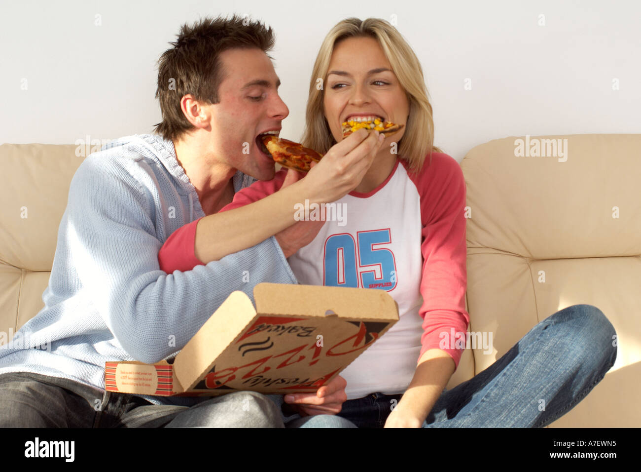 couple sitting on sofa eating a pizza cozy night in take away Stock