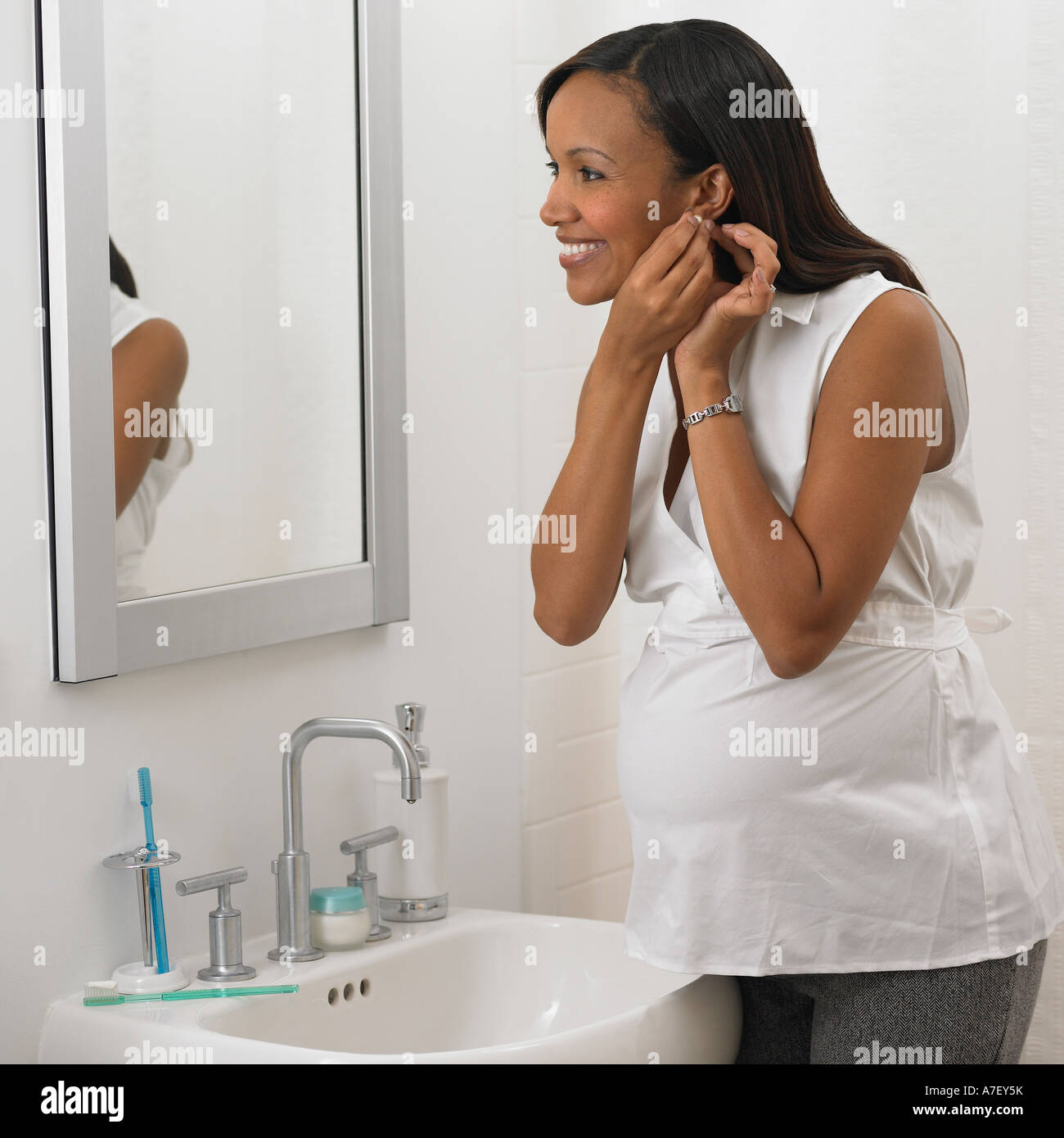 Pregnant African woman putting on earring in bathroom Stock Photo