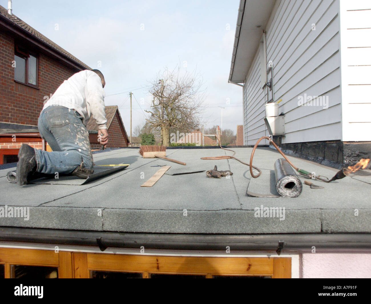 Roofer On Knees Laying New Bitumen Felt On Flat Garage Roof