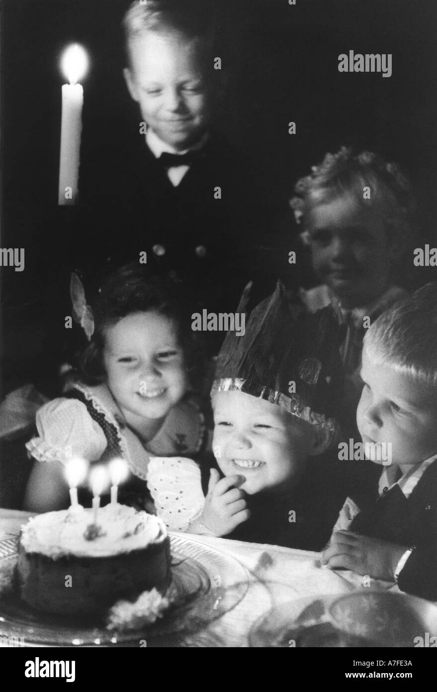 Young child prepares to blow out the candles on his birthday cake while brother sister and friends look on Stock Photo