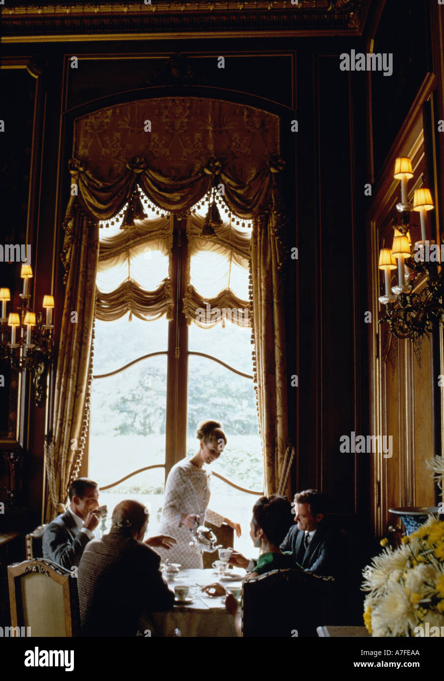 Female hostess serving tea to a group of businessmen talking at a table