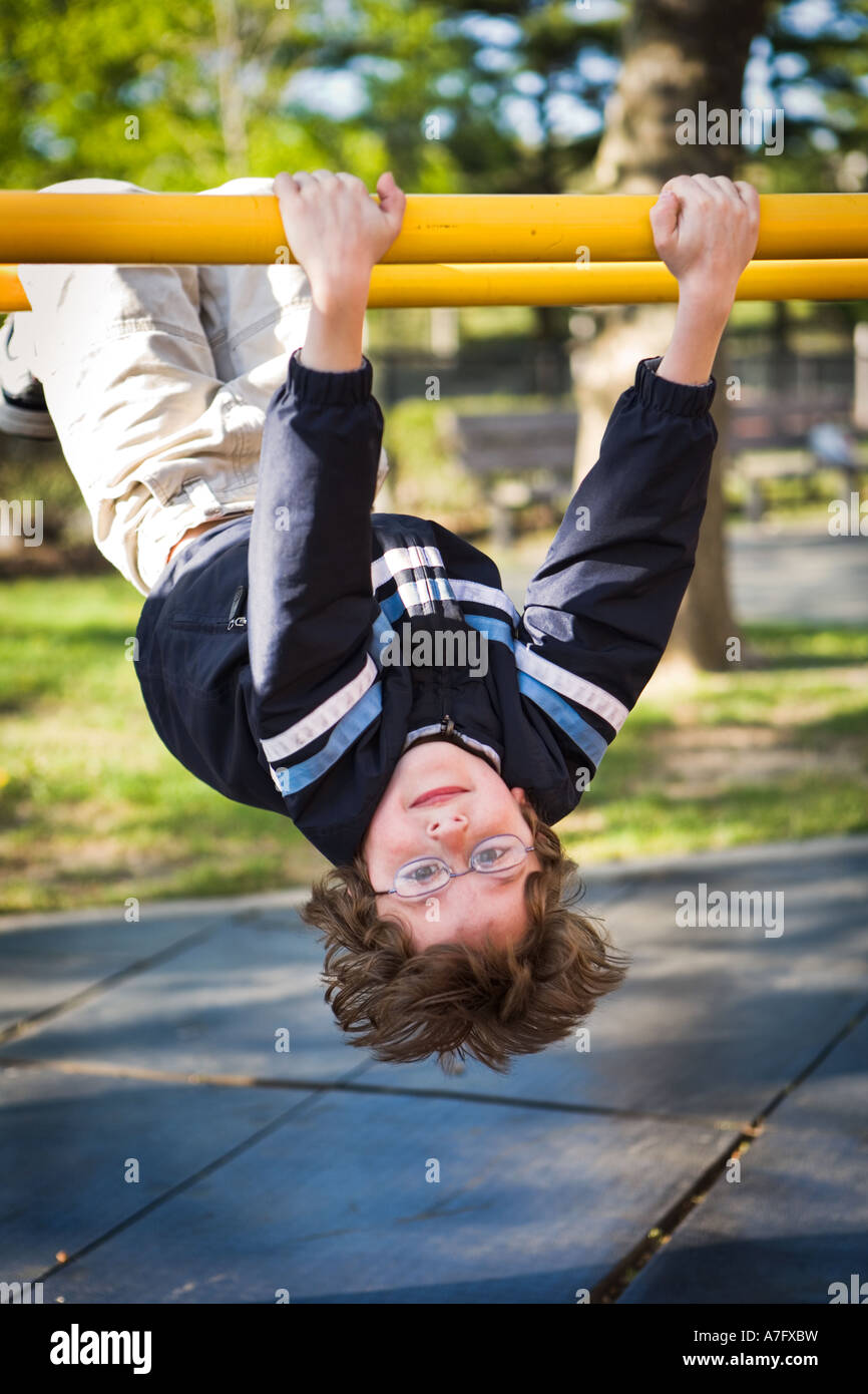 young boy playing hanging upside down at playground parallel bars Stock Photo