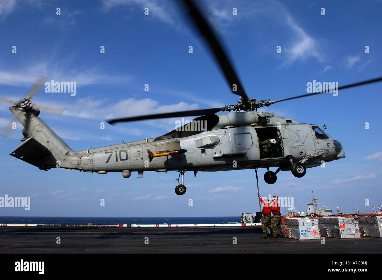 An air crewman watches as two aviation ordnancemen connect transport cables to a SH-60B helicopter. Stock Photo